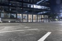 an empty parking lot in front of a building at night with buildings behind it and stairs