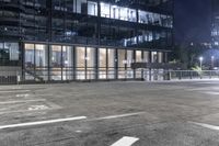 an empty parking lot in front of a building at night with buildings behind it and stairs