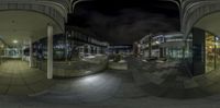 the 360 - view image is reflecting different buildings in the night time photo, a black sky and a building in the background