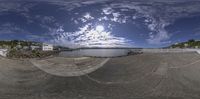 a fisheye panoramic photo of a skate park on water front with sun reflecting in