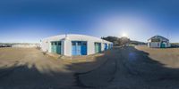 a group of small buildings in a large parking lot and sun shining down on the blue sky