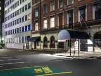 a city street with a few buildings and an umbrella on the corner at night,