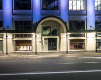 a building with several doors lit up at night and empty roads to the side of it