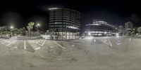 an empty skate park with several buildings in the background and light on either side of it