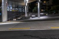 a sidewalk under an overpass at night with stairs and steps up to it in the foreground