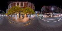 a spherical panorama photo of an urban street with buildings and trees in the background at night