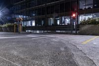 an empty parking lot with some traffic lights and a large building in the background at night