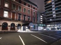 a street at night with a parking lot and building behind it and lights on the windows