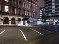 a street at night with a parking lot and building behind it and lights on the windows