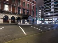 a street at night with a parking lot and building behind it and lights on the windows