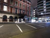 a street at night with a parking lot and building behind it and lights on the windows