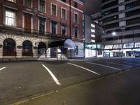 a street at night with a parking lot and building behind it and lights on the windows