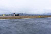 a wet runway with a field and buildings on it during the day in cloudy weather