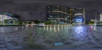 circular sculpture of circular shapes in city at night time, with buildings reflected in the background