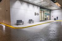 a few benches are sitting on the curb outside a building at night time outside, a city sidewalk, and a large door