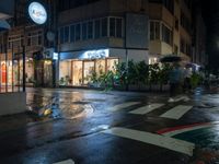 a wet city street in the rain at night with a store with shops and plants in the windows