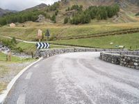 a rural road in the middle of mountains with a road sign hanging from it's sides