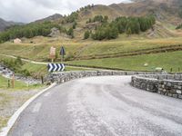 a rural road in the middle of mountains with a road sign hanging from it's sides