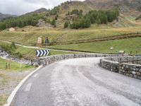 a rural road in the middle of mountains with a road sign hanging from it's sides