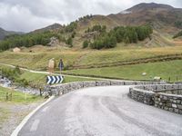 a rural road in the middle of mountains with a road sign hanging from it's sides