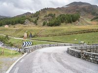 a rural road in the middle of mountains with a road sign hanging from it's sides