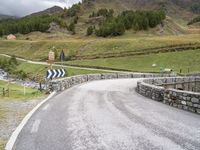 a rural road in the middle of mountains with a road sign hanging from it's sides