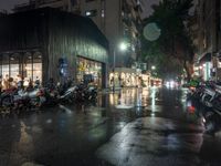 a bunch of motorcycles parked on the street at night on a rainy sidewalk in a busy city