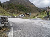 a winding mountain side road with a sign on the left and a stone wall on the right