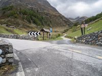 a winding mountain side road with a sign on the left and a stone wall on the right