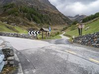 a winding mountain side road with a sign on the left and a stone wall on the right