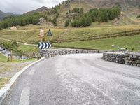 a large rock wall next to the road with mountains in background on cloudy day near water