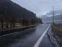 a wet road with a mountain in the background in a rural town area, and lots of trees