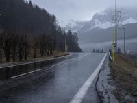 a wet road with a mountain in the background in a rural town area, and lots of trees