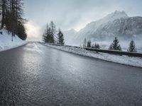 the wet road that runs into the snowy hills of mountains and pine trees are present