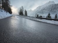 the wet road that runs into the snowy hills of mountains and pine trees are present