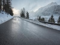 the wet road that runs into the snowy hills of mountains and pine trees are present
