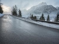 the wet road that runs into the snowy hills of mountains and pine trees are present