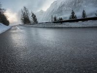 the wet road that runs into the snowy hills of mountains and pine trees are present