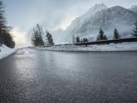 the wet road that runs into the snowy hills of mountains and pine trees are present