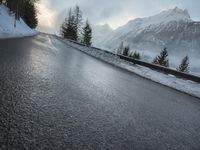 the wet road that runs into the snowy hills of mountains and pine trees are present