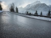 the wet road that runs into the snowy hills of mountains and pine trees are present