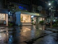 a wet road with a small store next to it and the neon light above the buildings