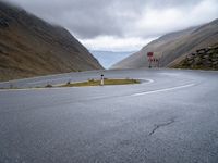 a curving curved road next to a mountain pass under a cloudy sky and clouds on a grey cloudy day