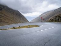 a curving curved road next to a mountain pass under a cloudy sky and clouds on a grey cloudy day