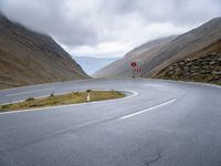 a curving curved road next to a mountain pass under a cloudy sky and clouds on a grey cloudy day