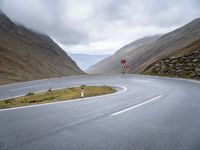 a curving curved road next to a mountain pass under a cloudy sky and clouds on a grey cloudy day