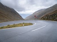 a curving curved road next to a mountain pass under a cloudy sky and clouds on a grey cloudy day