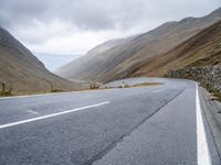 a motorcycle sits parked on a mountain road with a view across the mountains and the roadway