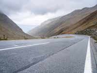 a motorcycle sits parked on a mountain road with a view across the mountains and the roadway