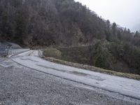 a wet road with gravel on the side and a train coming down the hill below